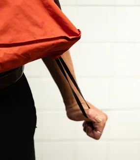 The orange tote carried over the shoulder against a white tiled wall